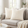 A cream faux fur stripe decorative throw pillow cover resting on a light gray sofa.