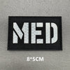 Black woven patch with white capitalized letters MED on a gray background