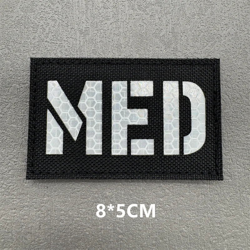 Black woven patch with white capitalized letters MED on a gray background