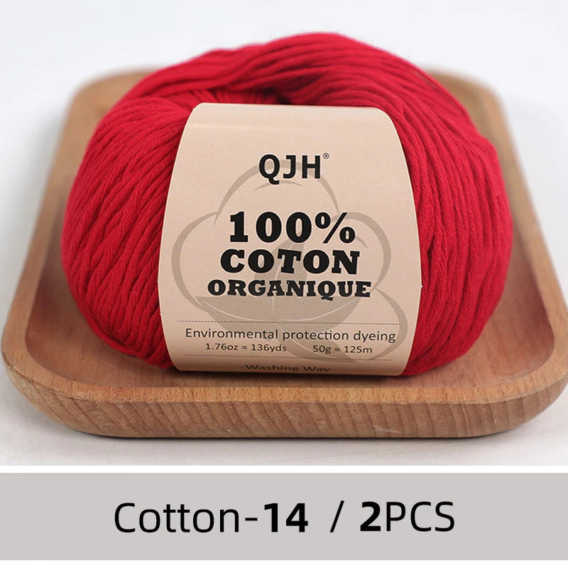 A ball of red organic cotton yarn labeled QJH 100% COTON ORGANIQUE resting on a wooden tray.