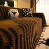 A close-up of a brown herringbone chenille sofa cover with black geometric patterns and a white tassel accent pillow.