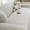 A light beige stretch jacquard sofa slipcover in a living room setting with a decorative knitted pillow.