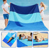 A large, multi-colored foldable waterproof outdoor picnic mat is shown being used on a beach with people.