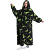 A woman wearing a black hoodie blanket featuring green dinosaur and palm tree patterns.