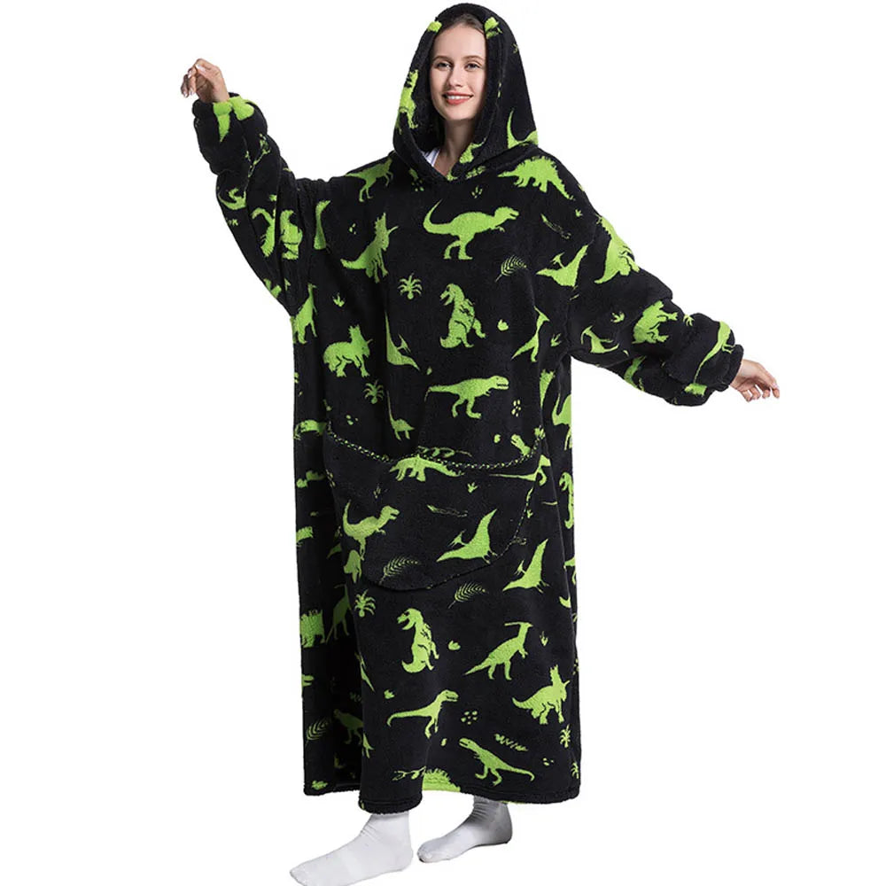 A woman wearing a black hoodie blanket featuring green dinosaur and palm tree patterns.