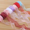 A collection of sheer satin ribbons in shades of pink, red, and blue are rolled and draped on a wooden surface.
