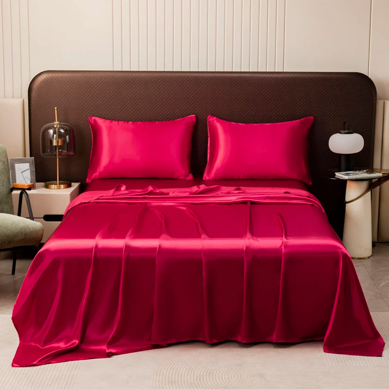 A luxurious magenta satin flat bed sheet set with two pillows is displayed on a bed against a dark brown headboard.
