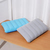 A light blue inflatable travel pillow and a gray inflatable travel pillow resting on a wooden table.