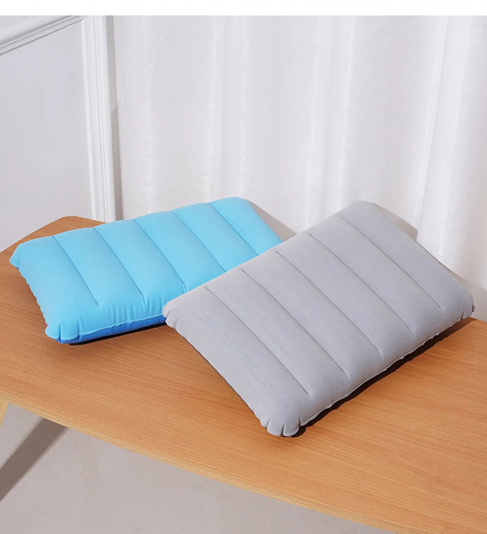A light blue inflatable travel pillow and a gray inflatable travel pillow resting on a wooden table.