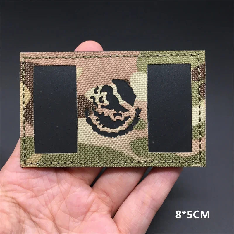 A rectangular tactical patch featuring a national flag emblem on a camouflage background, held in a hand.