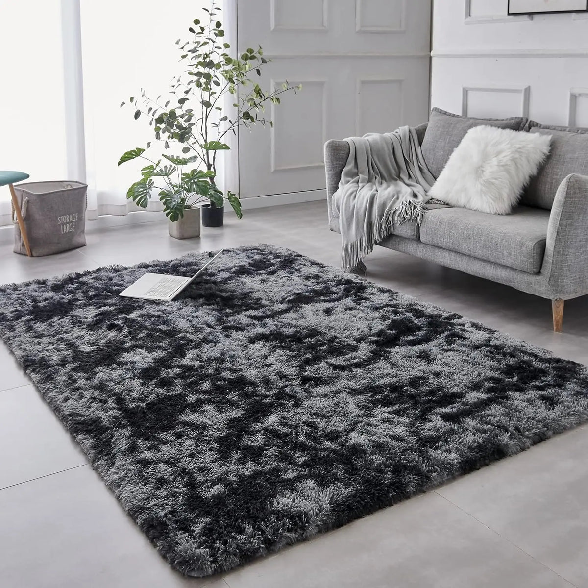 A dark gray tie-dyed plush floor mat placed on a light floor in a modern living room setting.