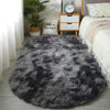 A dark gray plush floor mat placed on a light wood floor next to a white bed and a wooden nightstand.