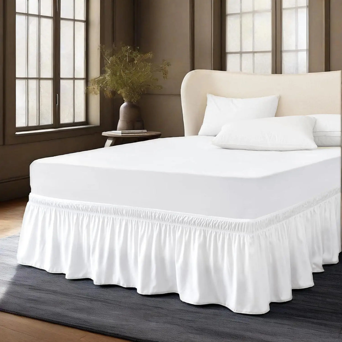 A white bed with a ruffled skirt and white pillows on a dark gray floor.