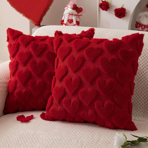 Two textured red knitted heart-shaped cushions resting on a white sofa.