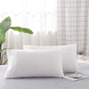 A set of two white soft polyester pillow covers lying on a gray surface.