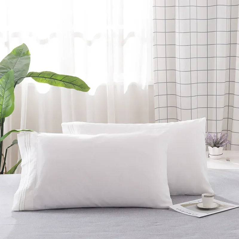 A set of two white soft polyester pillow covers lying on a gray surface.