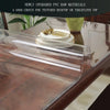 A clear PVC table protector mat is placed on a wooden table, with stacked plates and cutlery nearby.