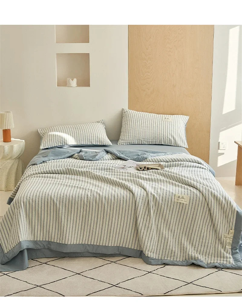 A light blue and white striped luxury jacquard summer quilt displayed on a bed with wooden paneling.