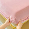 Hands are pulling up a pink flannel fitted sheet with deep pockets on a wooden bed frame.