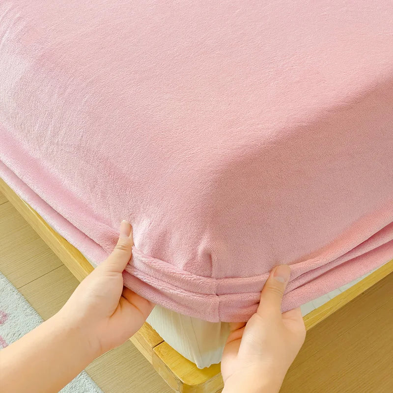 Hands are pulling up a pink flannel fitted sheet with deep pockets on a wooden bed frame.