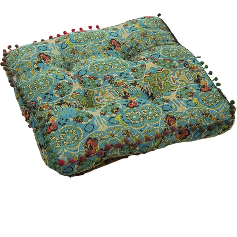 A square throw cushion with a blue and green bohemian patterned fabric and fringed edges.
