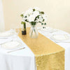 A golden sequin table runner on a white tablecloth with white floral arrangements and place settings.