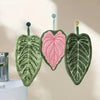 Three hand towels shaped like leaves in shades of green and pink hanging on a wall