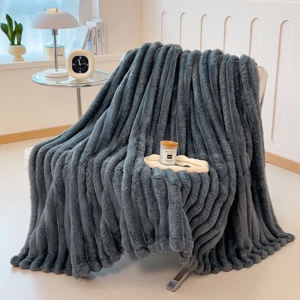 A thick, gray, fuzzy blanket is draped in a vertical pile on a light-colored surface.