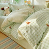 A light green and white gingham duvet and pillow set with small orange accents on a bed.