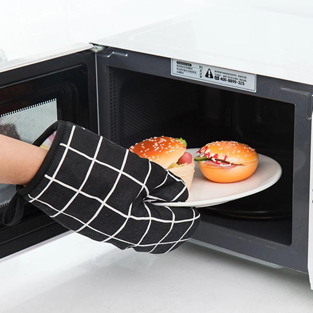 A hand wearing a black checkered oven glove is reaching into an open white kitchen oven to retrieve a food item.
