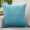A square teal velvet cushion cover resting on a light-colored sofa.