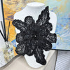 Black floral lace applique fabric patches with sequins displayed on a white mannequin against an abstract yellow and blue bac