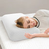 A woman rests her head on a white memory foam neck pillow with a light-colored shirt.