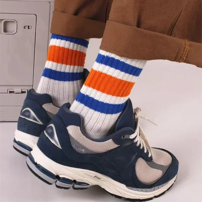 A pair of navy blue athletic shoes paired with striped crew socks featuring white, orange, and blue bands.