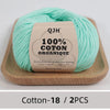 A ball of light mint green organic cotton yarn labeled QJH 100% COTON ORGANIQUE resting on a wooden tray.
