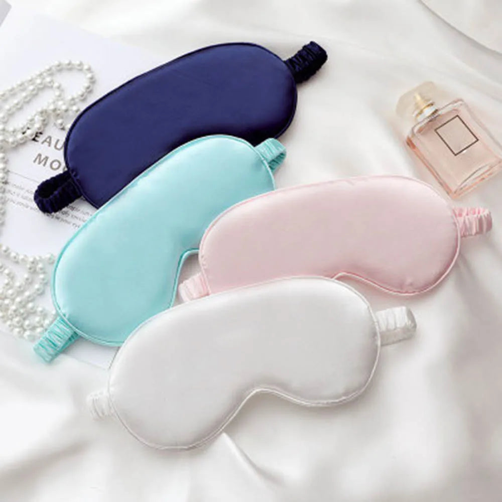 A collection of silk sleep masks in various colors including navy blue, light blue, pink, and white resting on a white fabric
