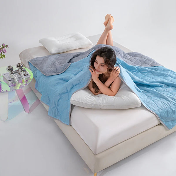 A woman is relaxing on a bed covered with a blue breathable cooling blanket and white pillows.