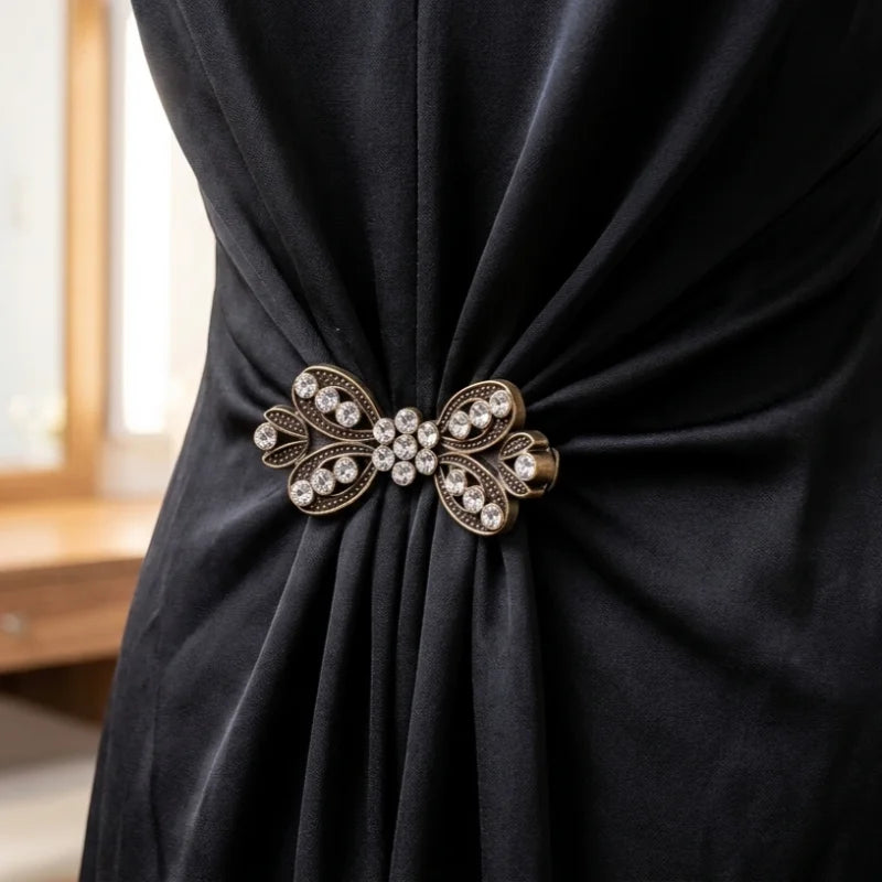 A close-up of a black fabric draped with an elegant gold rhinestone clothing clip.