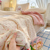 A close-up of a pink floral quilt draped over a bed, with a hand holding the fabric.