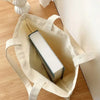 A beige canvas shopping bag with light-colored handles and a rectangular white item inside, resting on a wooden surface.