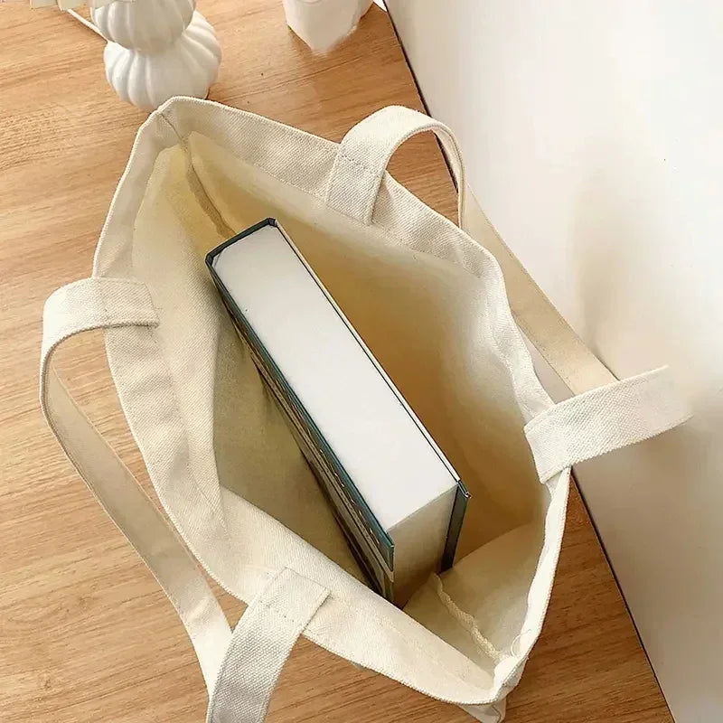 A beige canvas shopping bag with light-colored handles and a rectangular white item inside, resting on a wooden surface.