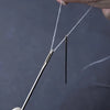 A hand is holding a stainless steel hand sewing needle with a white thread, demonstrating the product.