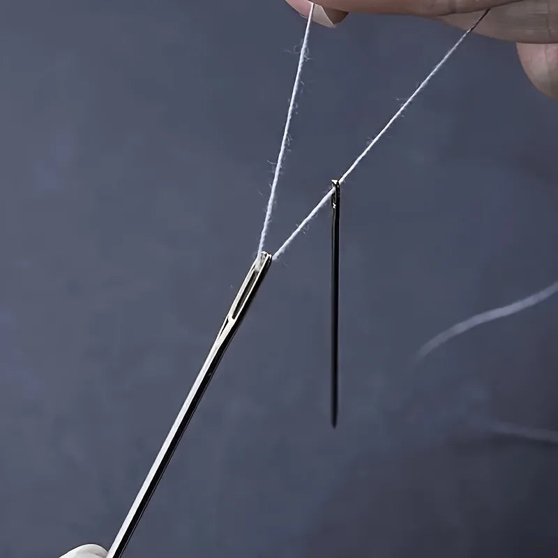 A hand is holding a stainless steel hand sewing needle with a white thread, demonstrating the product.