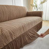 A beige jacquard stretch sofa cover draped over a modern sofa in a bright room.