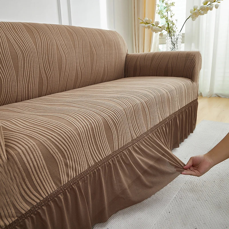 A beige jacquard stretch sofa cover draped over a modern sofa in a bright room.