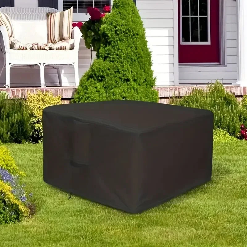A dark gray waterproof fire pit cover with a drawstring lying on a green lawn in front of a house.