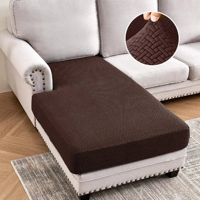 A dark brown jacquard stretch sofa cushion cover placed on a light gray sofa and a rug.