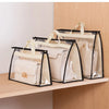 A set of clear and black dustproof storage bags for handbags displayed on a wooden shelf.