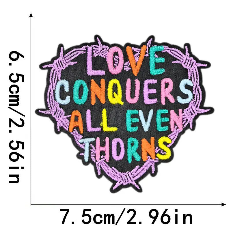 Black embroidered patch with purple and yellow text that reads LOVE CONQUERS ALL EVEN THORNS