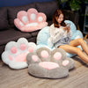 A woman is relaxing on a dark sofa surrounded by several pink and white plush bear paw cushions.